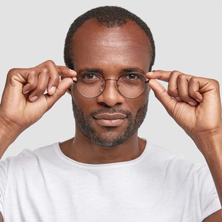 Young confident dark skinned male with stubble, keeps hands on spectacles, serious expression and intention to do something